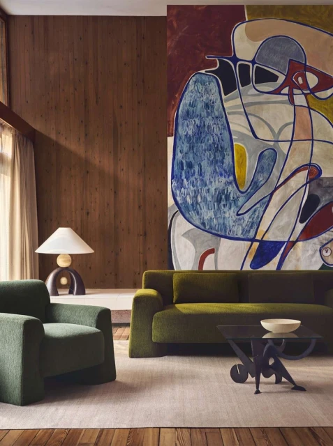 Living room interior with green sofa and armchair, featuring a large abstract painting on the wall and modern lighting, indoor setting.