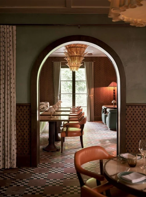 Ornate restaurant interior featuring tables with orange chairs, an archway, checkered floors, patterned walls, and a hanging chandelier.
