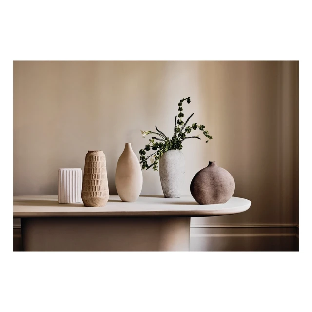 Still life of five ceramic vases, varying in shape and texture, displayed on a neutral-colored table against a beige wall in a studio setting.