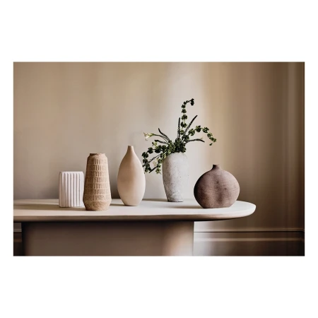 Still life of five ceramic vases, varying in shape and texture, displayed on a neutral-colored table against a beige wall in a studio setting.