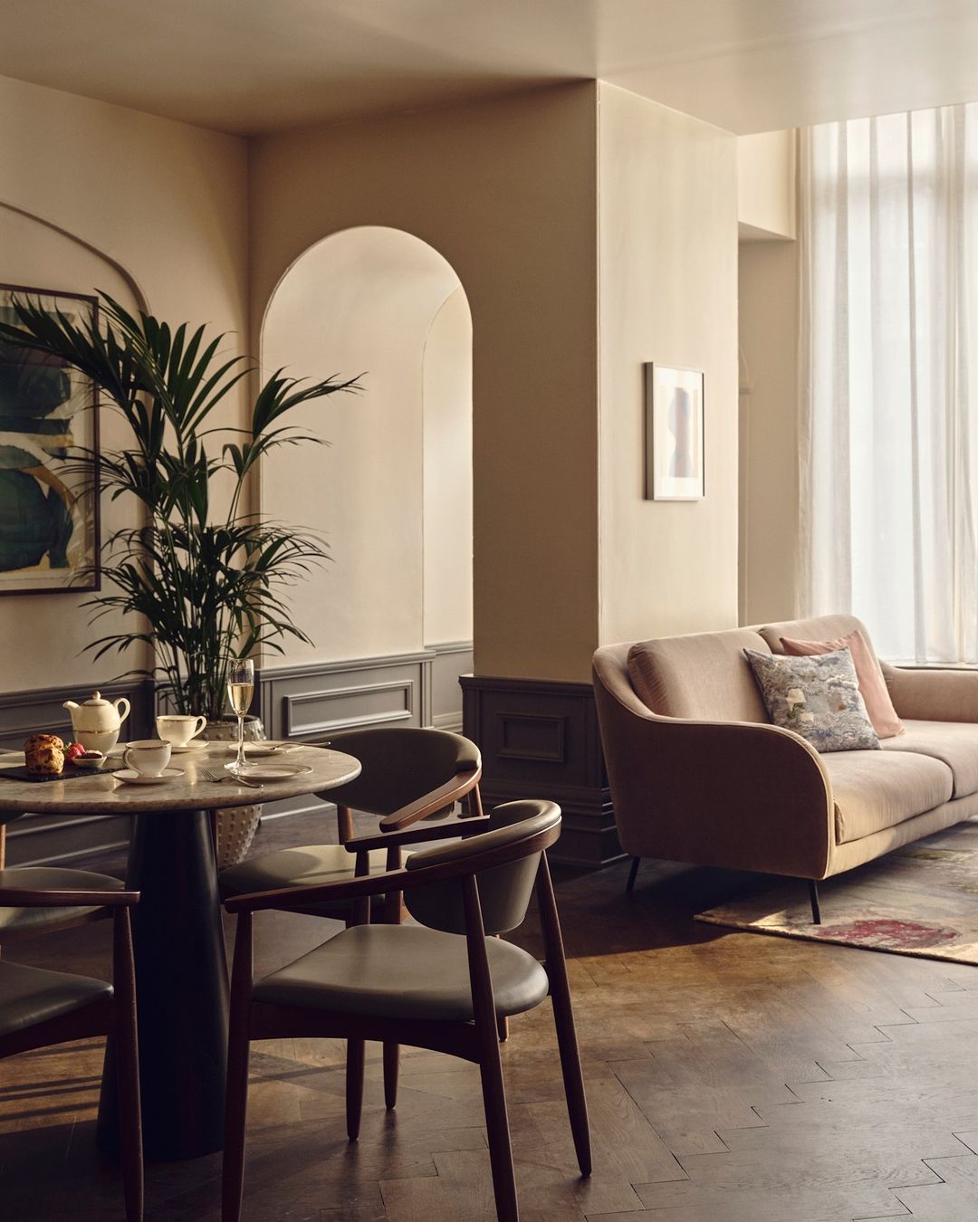 Interior view of a home with chairs around a table, a potted plant, and a couch under bright window light. Minimalist design.