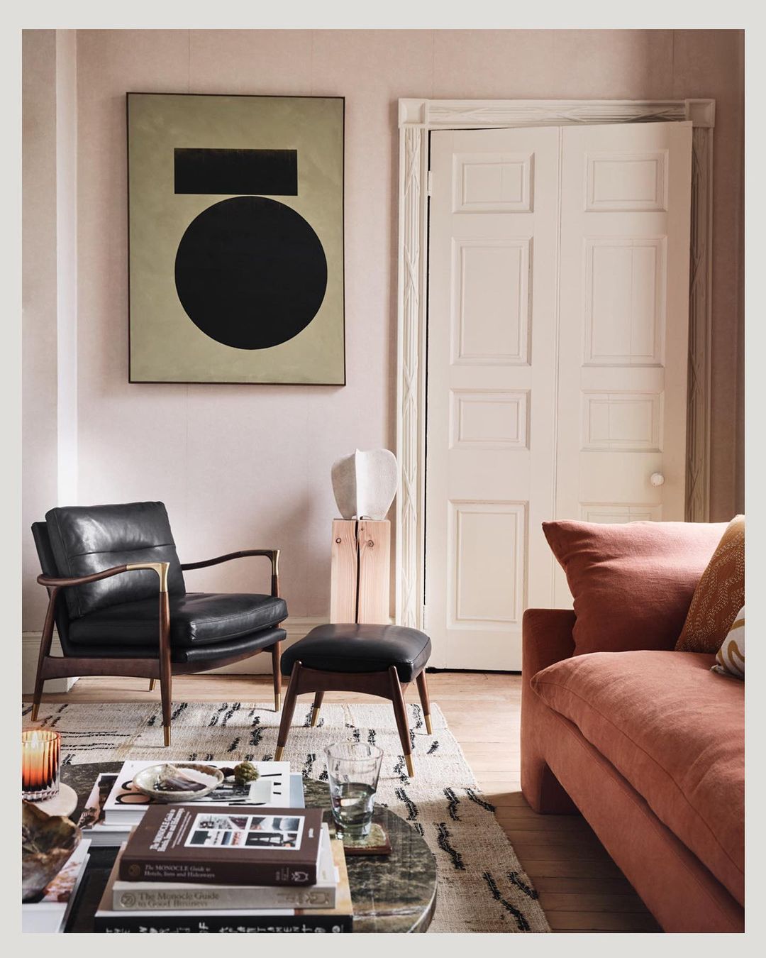 Living room interior featuring black leather armchair, ottoman, and sofa with a geometric art piece in a neutral, contemporary setting.