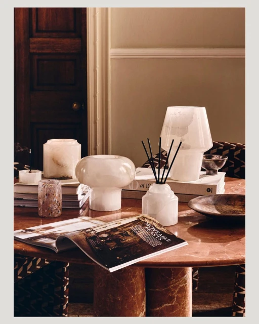 Interior scene featuring decorative alabaster lamps and a diffuser, styled on a red marble table with books and a magazine. Home decor.