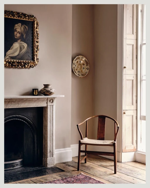 Interior design featuring a vintage painting, fireplace, wooden chair, and decorative dish in a room with light brown walls and wood floor.