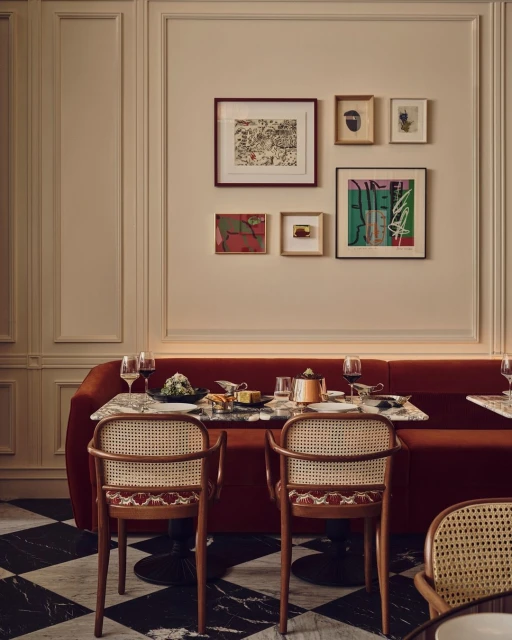 Dining area with a red booth, marble floors, rattan chairs, and a wall featuring framed artwork, offering a cozy restaurant setting.