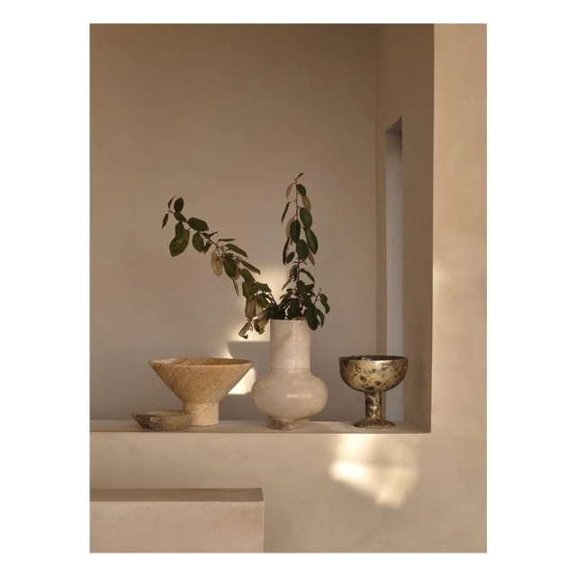 Interior shot featuring a selection of decorative vases and green leafy branches arranged on a shelf in a minimalist setting.