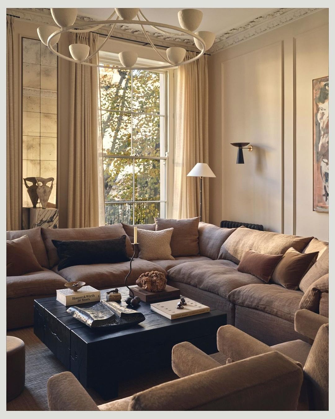 Living room interior featuring a large sectional sofa, dark wood coffee table with decorative objects, and natural light from large window.