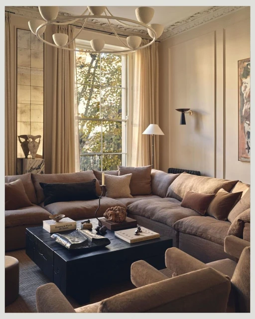 Living room interior featuring a large sectional sofa, dark wood coffee table with decorative objects, and natural light from large window.
