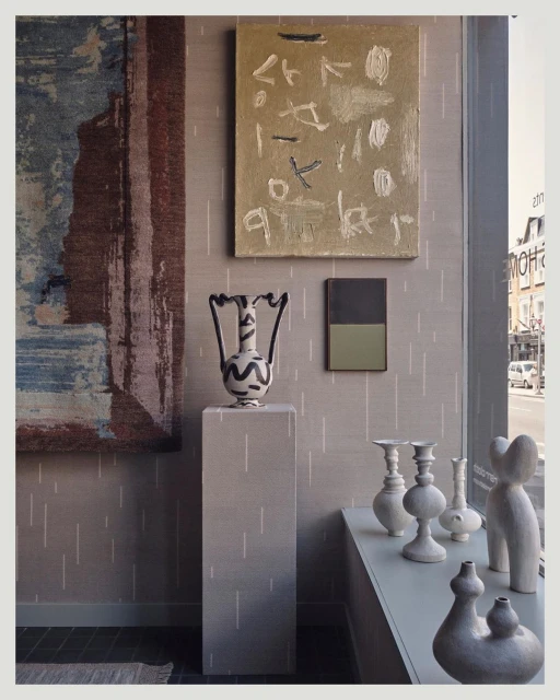 Interior space featuring neutral tones, abstract art, decorative vases, and a geometric pedestal, creating a modern, minimalist aesthetic.