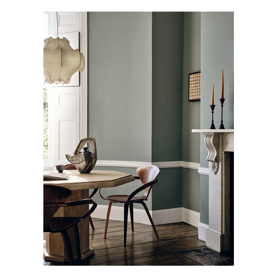 Dining room features olive green walls, hardwood floor, octagonal wood table with modern vase, chairs, and a white plaster fireplace.