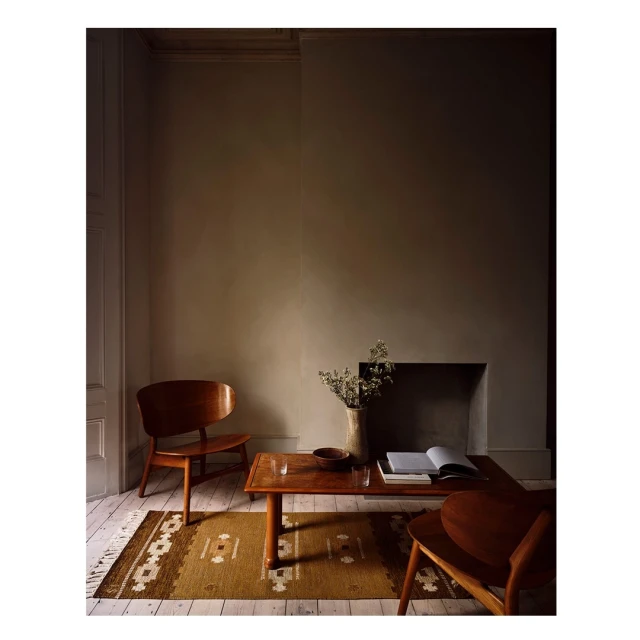 Cozy interior with brown wood chairs, square coffee table, vase with flowers, an open book, on a patterned tan rug and wood floor.