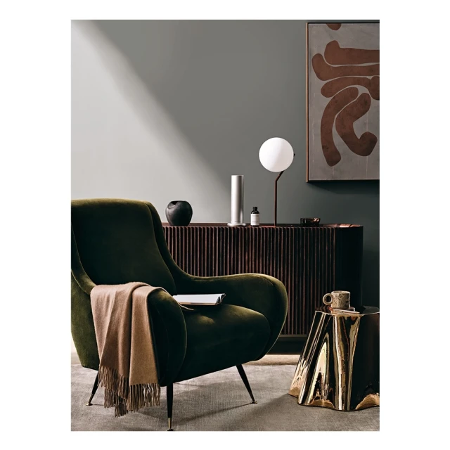 Interior photograph features a green armchair, a tan throw, and a brass side table with a lamp, vase, and decorative objects in a home setting.