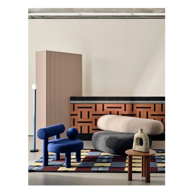 Interior design with a blue chair, rounded cushions, a geometric rug, and a wooden screen in a modern setting with neutral wall colors.