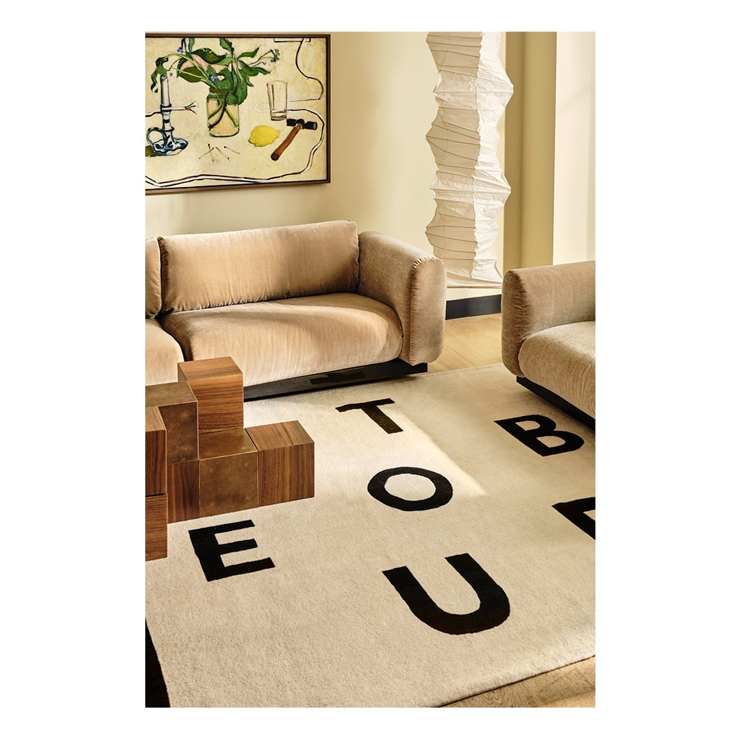 Beige sofa in a neutral-toned living room with modern art, decorative paper lantern, and alphabet rug in a stylish interior space.