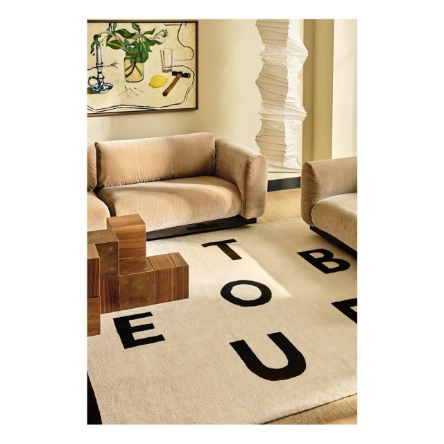 Beige sofa in a neutral-toned living room with modern art, decorative paper lantern, and alphabet rug in a stylish interior space.