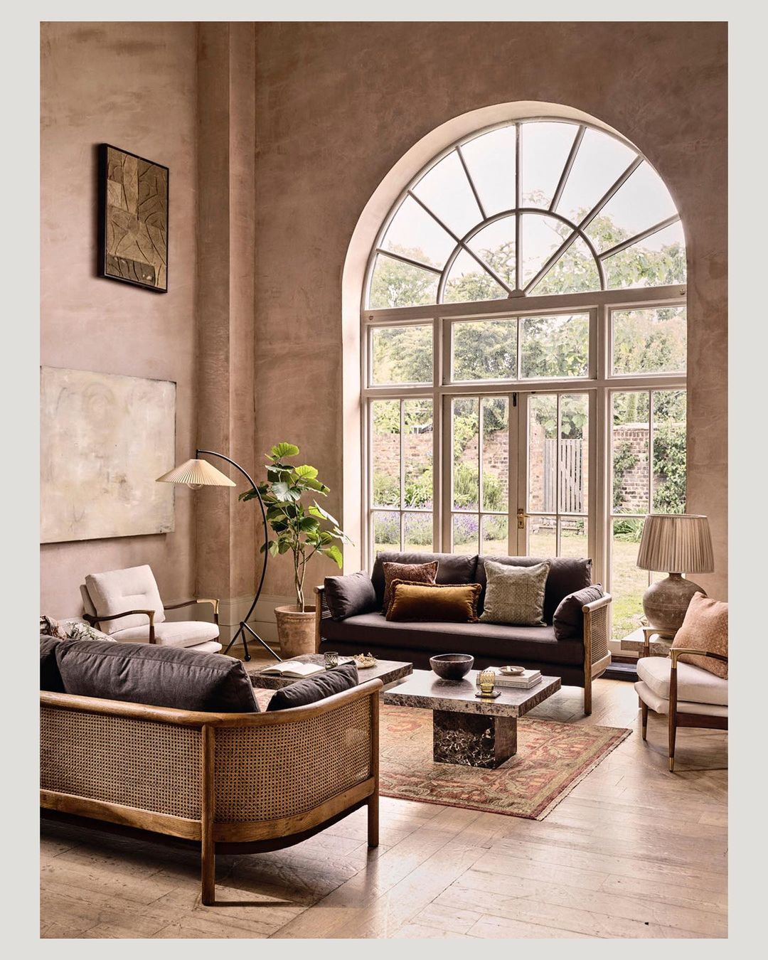 Living room interior with seating area, including sofas, chairs, a rug, and a coffee table, in a room with large windows and neutral tones.