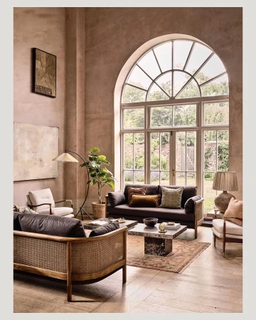 Living room interior with seating area, including sofas, chairs, a rug, and a coffee table, in a room with large windows and neutral tones.
