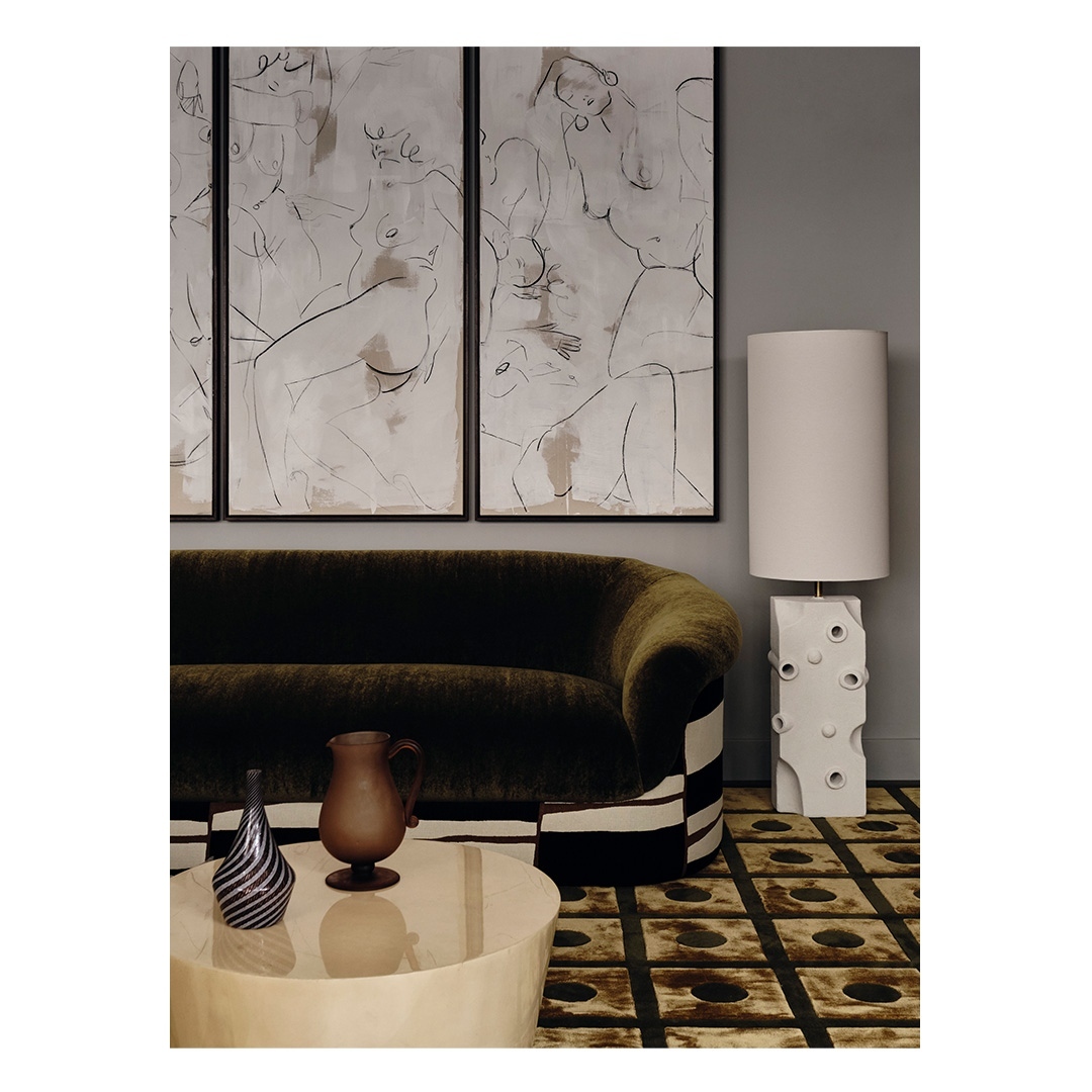 Interior view featuring a green velvet sofa, framed artwork, decorative vases on a table, and a distinctive lamp, creating an elegant ambiance.