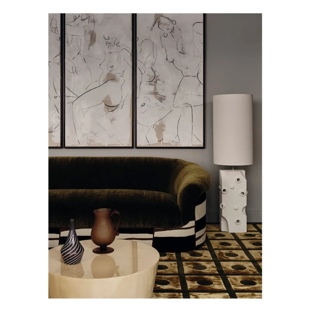 Interior view featuring a green velvet sofa, framed artwork, decorative vases on a table, and a distinctive lamp, creating an elegant ambiance.