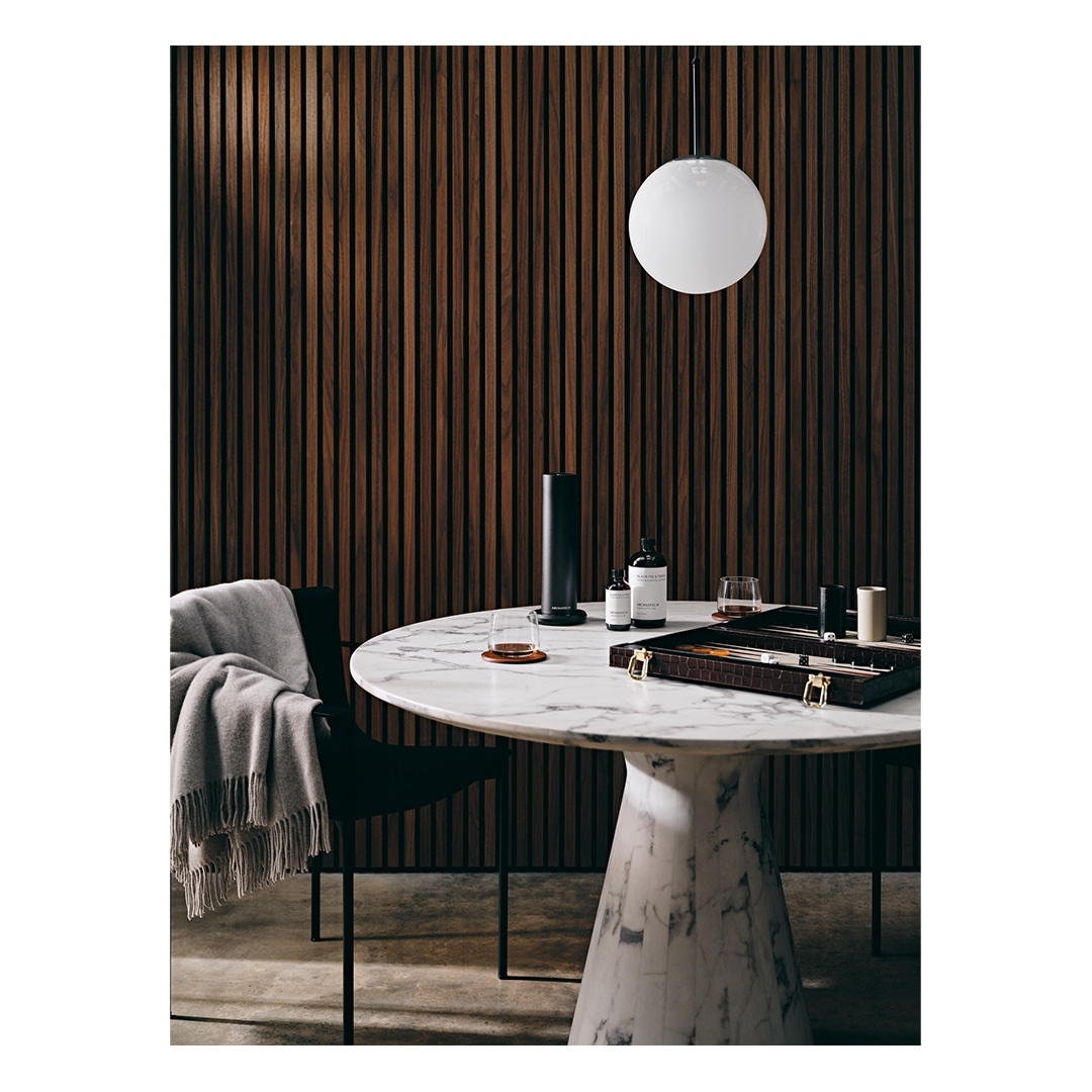 Interior shot of a marble table with decor, including diffuser, bottles, and game. The scene is lit by a spherical pendant light.