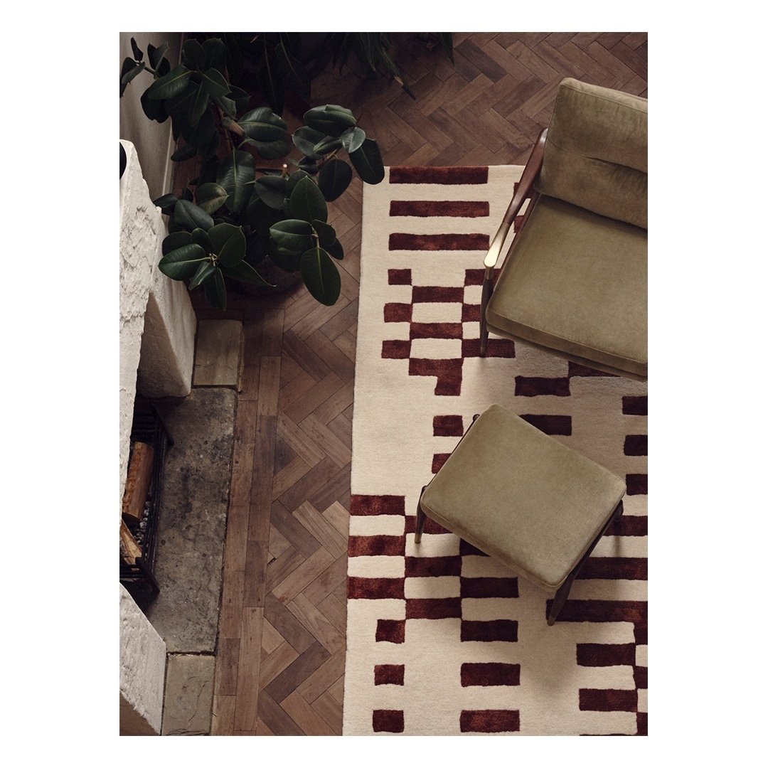Overhead shot of a modern cream and burgundy patterned wool rug, armchair, and ottoman in a minimalist living room with parquet flooring.
