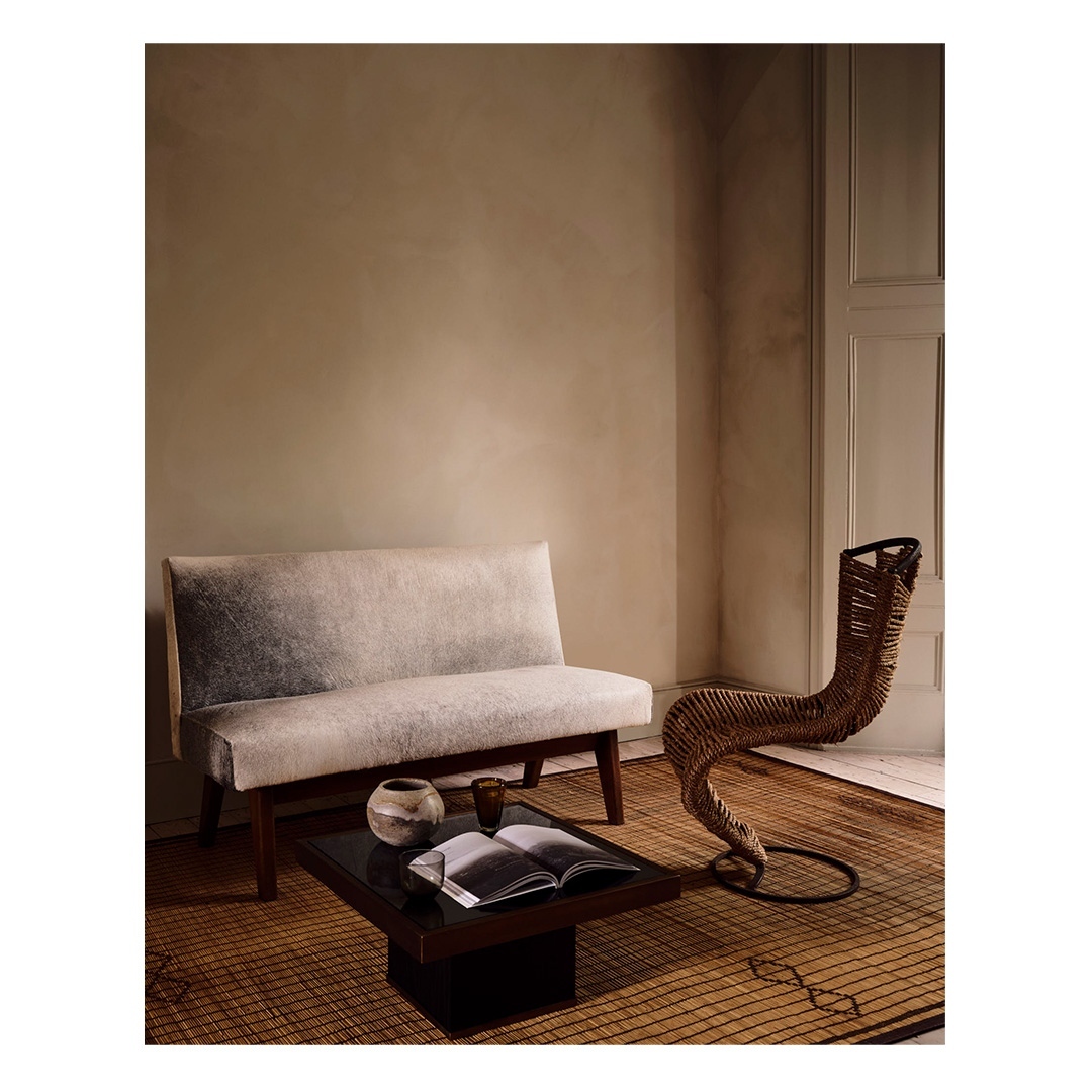 Interior design featuring a modern couch, unique woven chair, and dark coffee table with books in a room with neutral tones and soft lighting.