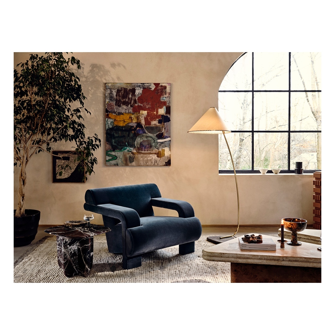 A dark blue upholstered armchair, modern floor lamp, and abstract painting inside a contemporary living room interior.
