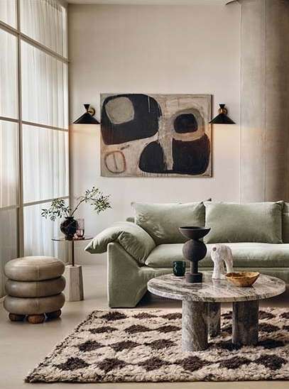 Living room interior with a light green sofa, round marble coffee table, abstract art, and a diamond-patterned rug on the floor.