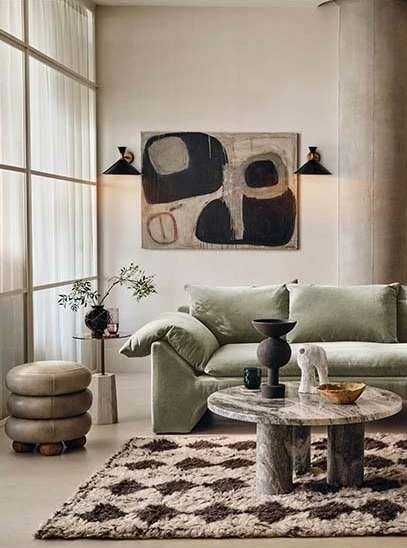 Living room interior with a light green sofa, round marble coffee table, abstract art, and a diamond-patterned rug on the floor.