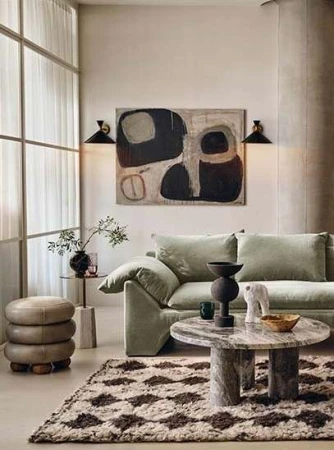 Living room interior with a light green sofa, round marble coffee table, abstract art, and a diamond-patterned rug on the floor.