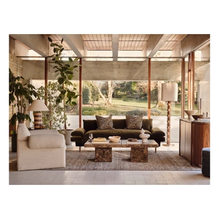 Living room interior with an olive green couch, patterned cushions, marble coffee table, lamps, a rug, and indoor plants.