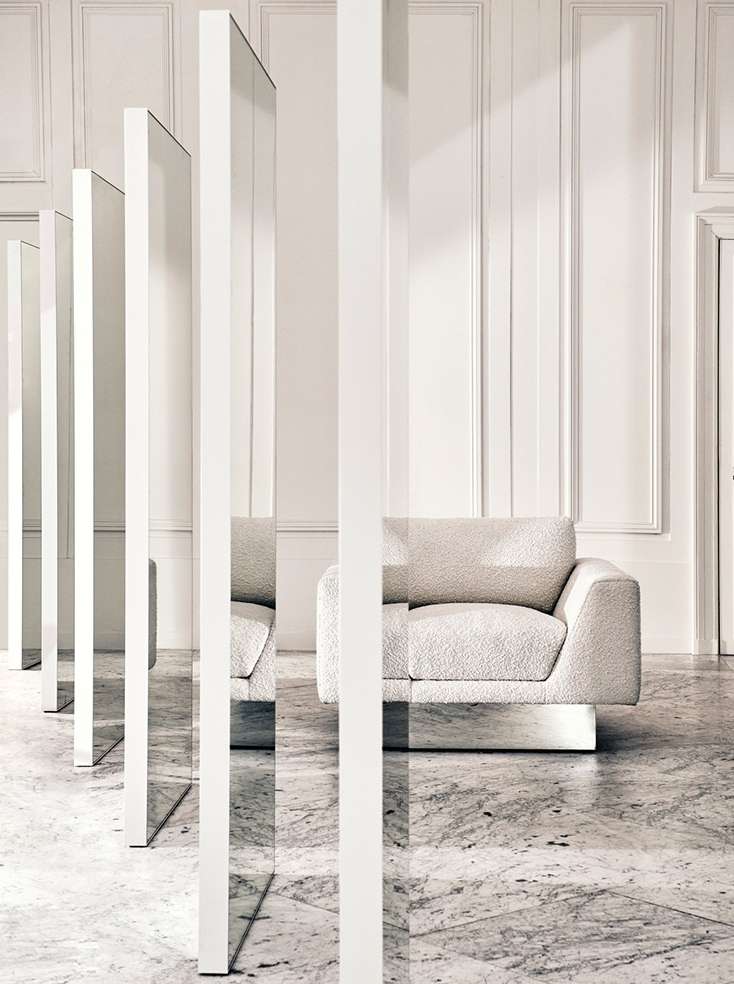 Modern interior design features a cream-colored armchair, white vertical panels, and marble flooring in a minimalist space with natural light.