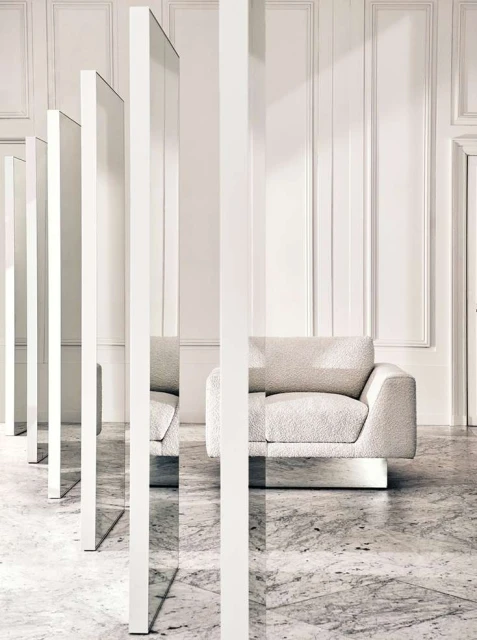 Modern interior design features a cream-colored armchair, white vertical panels, and marble flooring in a minimalist space with natural light.