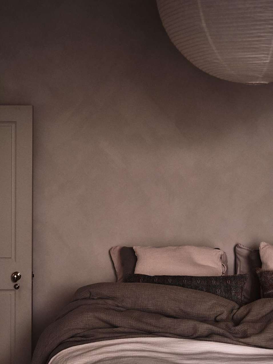 Tranquil bedroom interior featuring a cozy bed with multiple pillows and a lamp, set against a textured wall and a closed white door.