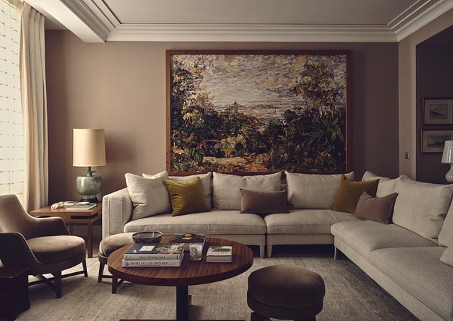 Interior design of a living room featuring a large corner sofa, round wood coffee table, lamp, painting, and upholstered chair.