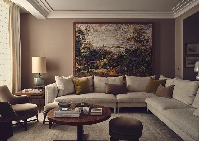 Interior design of a living room featuring a large corner sofa, round wood coffee table, lamp, painting, and upholstered chair.