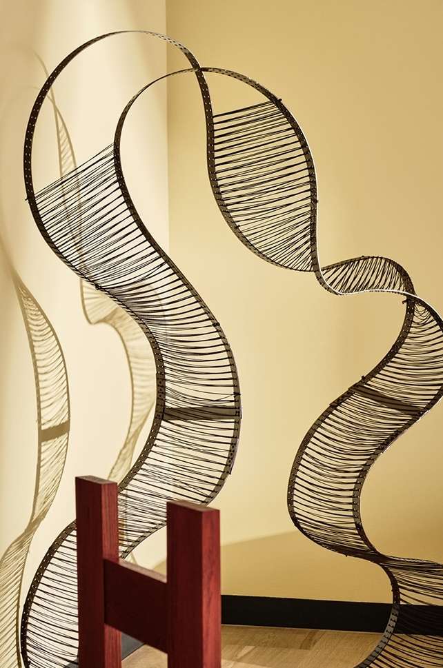 Abstract metal sculpture with S-curves creates a dynamic visual. The shadows cast on the cream-colored wall add depth to the composition.