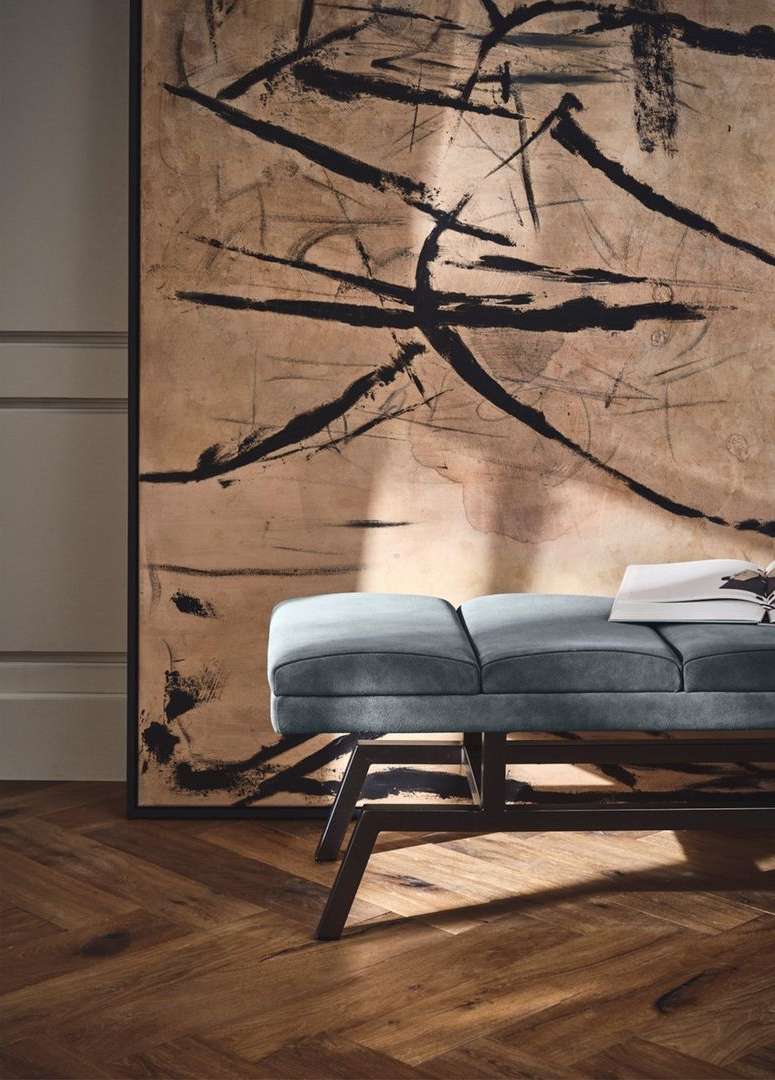 Interior design with a modern blue bench on a herringbone floor, set against an abstract painting in earth tones and black lines.