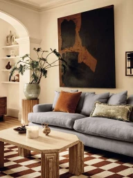 Living room interior featuring a grey sofa, large abstract painting, wooden coffee table, and a potted plant.