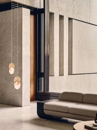 Modern interior with a neutral sofa, circular pendant lights, and large stone pillars in a spacious minimalist living area.