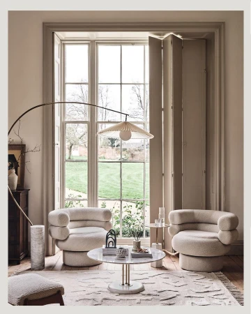 Two cream boucle armchairs surrounding a round marble coffee table in a bright living room by Ben Anders