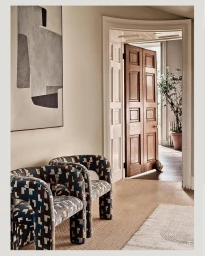 Two patterned armchairs in a neutral hallway with abstract artwork on the wall and wooden double doors open to another room