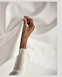 Close-up of a hand lifting white fabric against a light background, photographed by Ben Anders