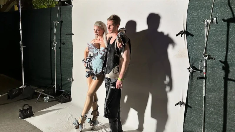 Fashion photo shoot features an adult male and female posing in avant-garde outfits against a white backdrop in a photo studio.