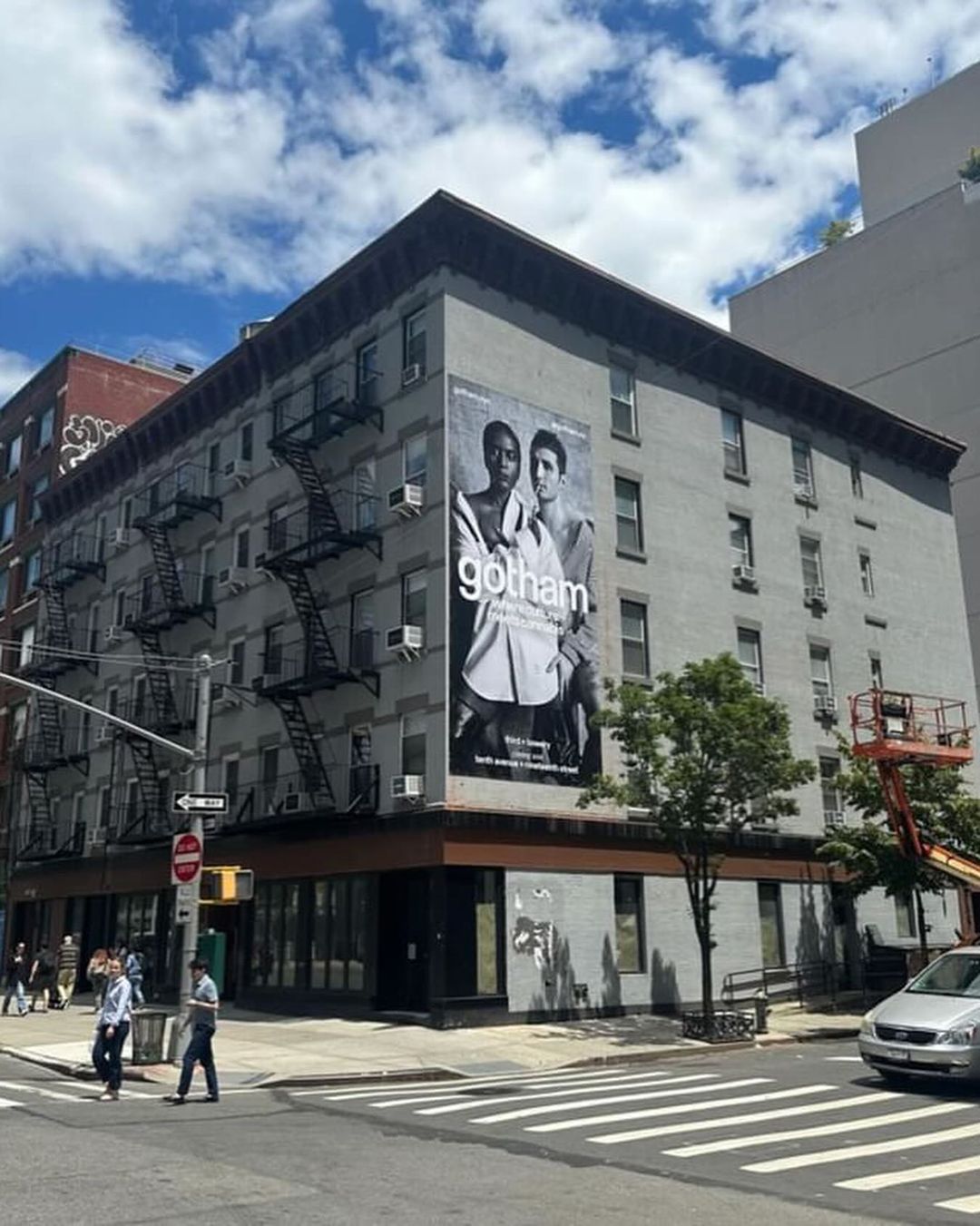 Exterior view of a gray apartment building featuring a large black-and-white advertisement for the TV show Gotham on its side.