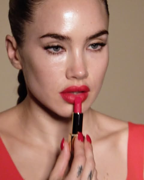 Close-up of a woman applying red lipstick, focusing on her face, hand holding the lipstick tube, and the red color palette.