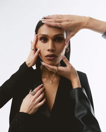 Portrait of a woman framed by hands wearing gold rings against a white seamless background