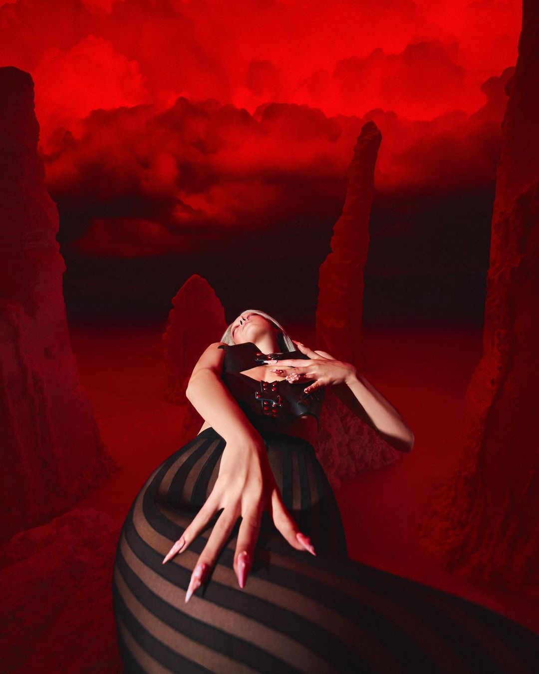 Surreal portrait of a woman in a black corset and striped skirt, posing against a backdrop of red rock formations and a cloudy sky.