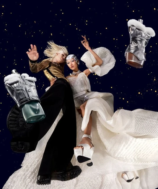 Two models wearing avant-garde fashion pose against a dark blue starry backdrop, showcasing futuristic styles and accessories. 