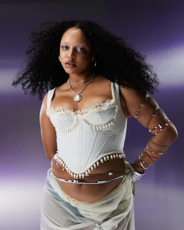 Portrait of a woman wearing a white lace corset top and layered pearl necklaces against a gradient purple background.